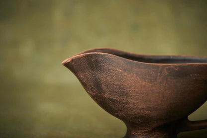 Handmade ceramic sauceboat or milk jug in rustic brown clay with green background
