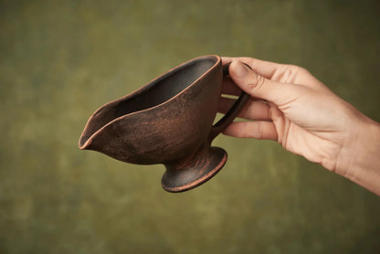 Hand holding a handmade ceramic sauceboat or milk jug with rustic brown finish