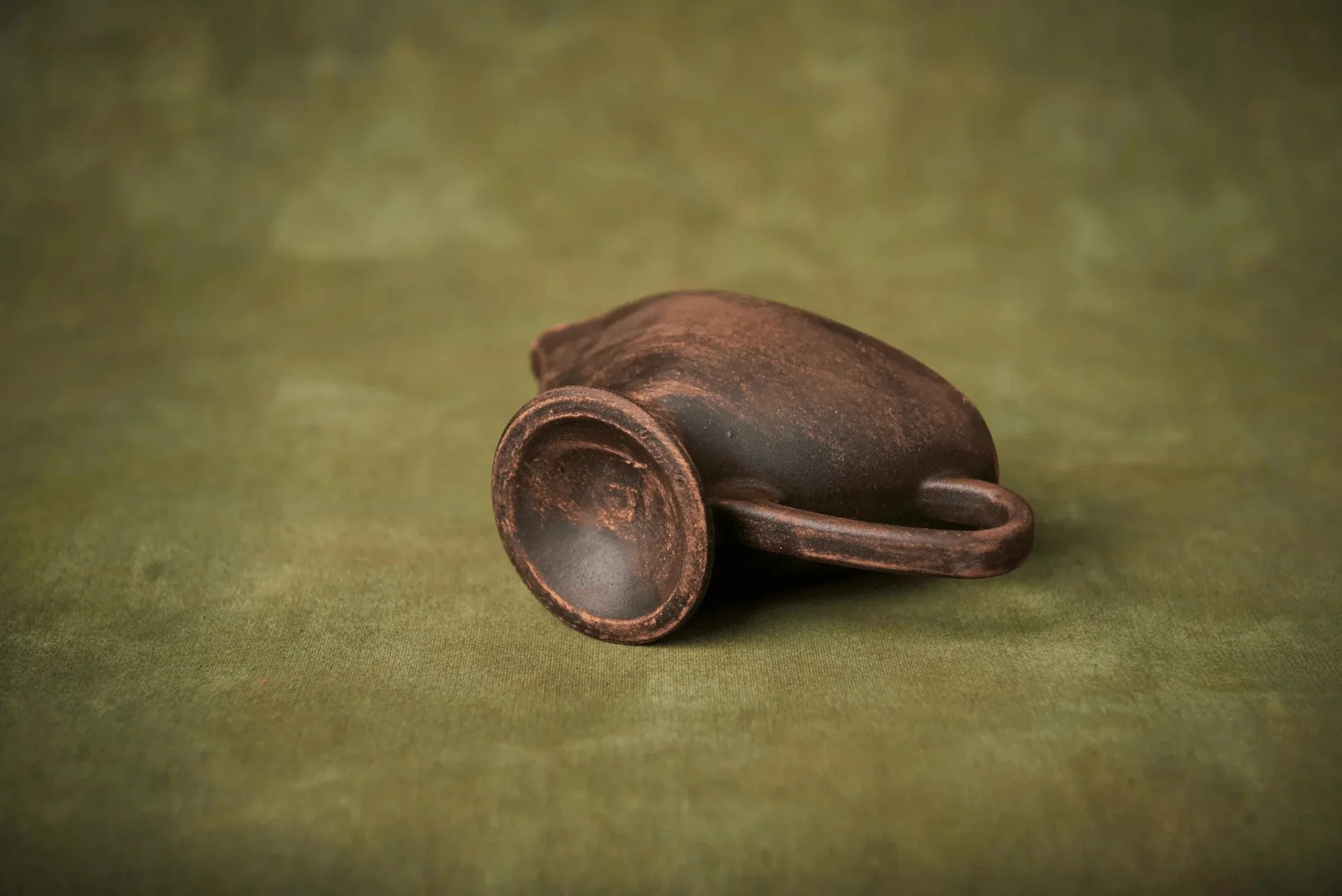 Handmade ceramic sauceboat milk jug with a rustic brown finish on green background
