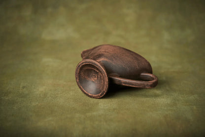 Handmade ceramic sauceboat milk jug with a rustic brown finish on green background