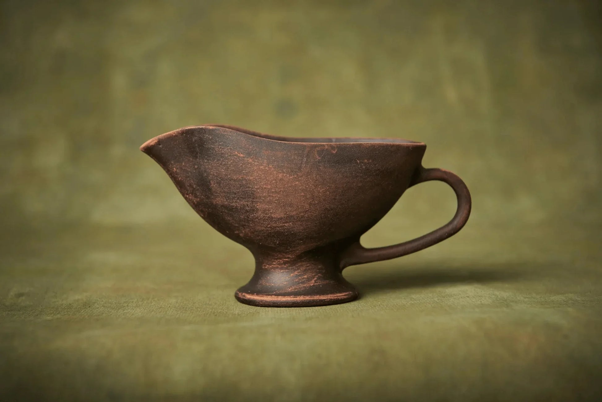 Handmade brown ceramic sauceboat on green fabric, artisan pottery homeware