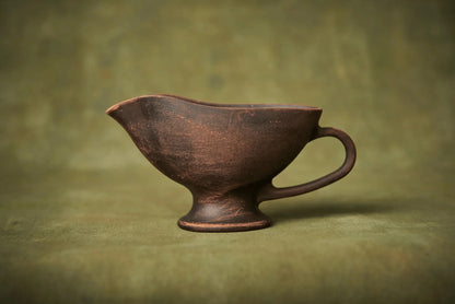 Handmade brown ceramic sauceboat on green fabric, artisan pottery homeware