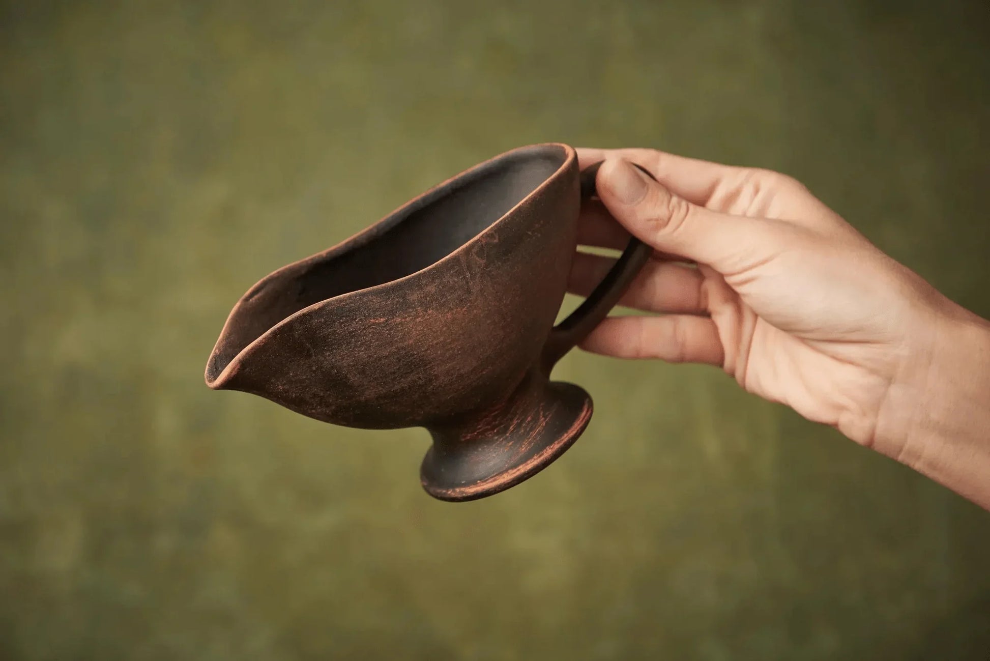 Hand holding a handmade ceramic sauceboat or milk jug with rustic brown finish