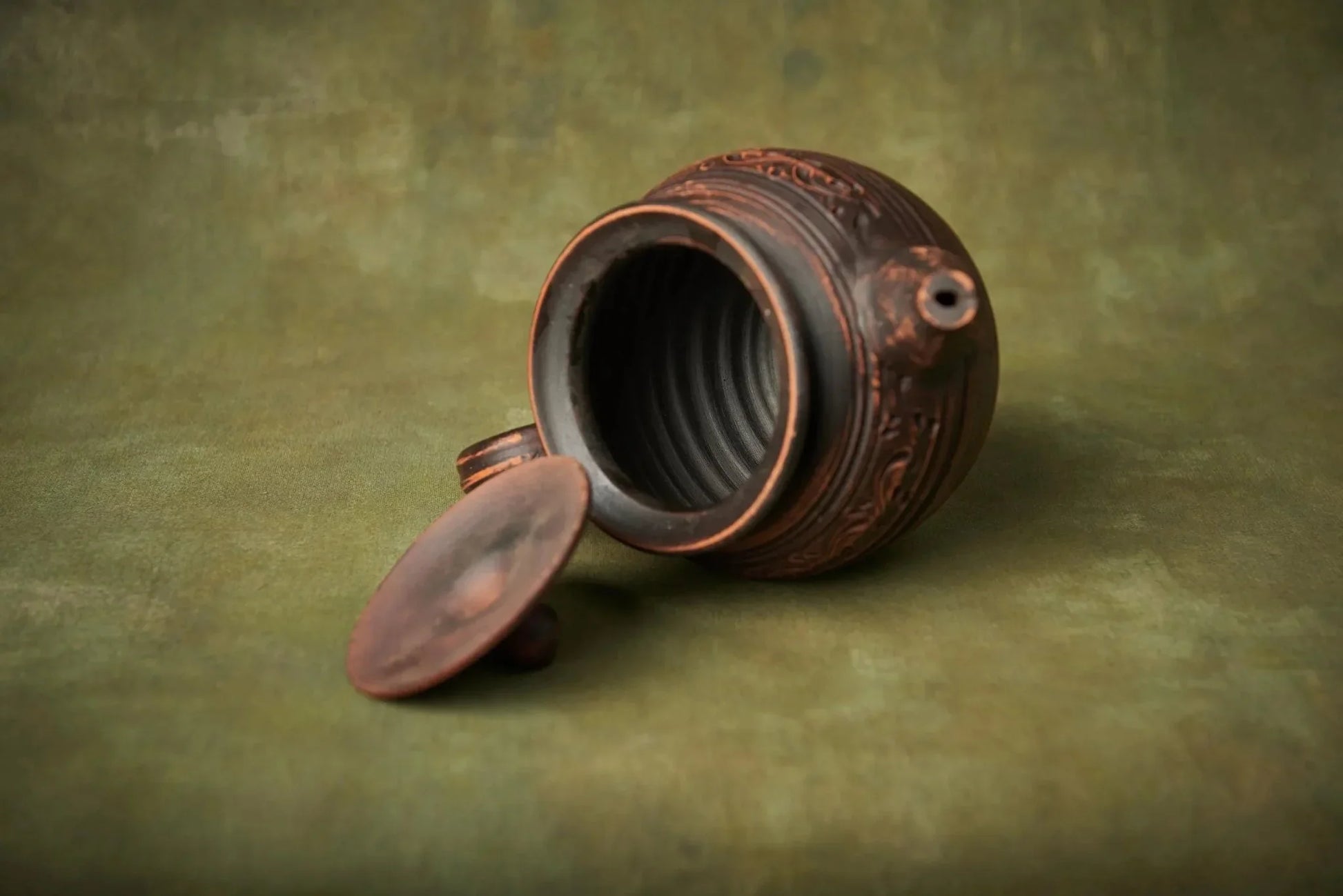 Handmade ceramic teapot with lid, engraved clay kettle on rustic green background