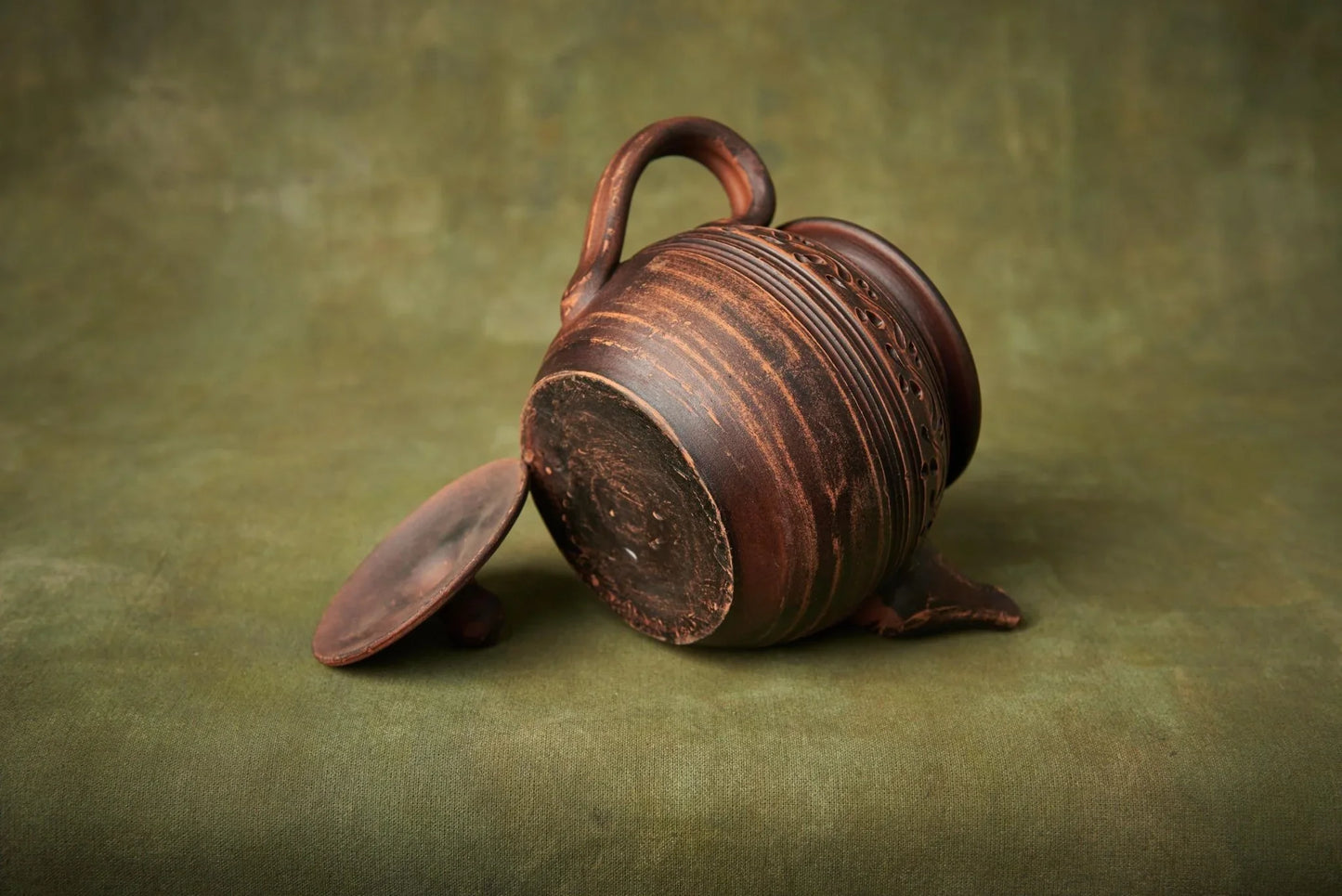 Handmade clay teapot with lid, unique engraved pottery, on green background
