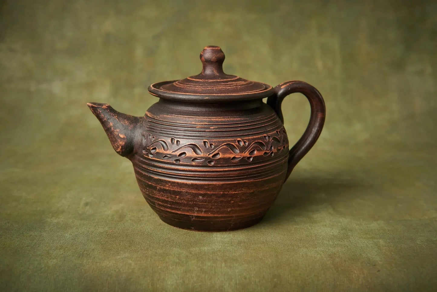 Handcrafted clay teapot with engraved patterns, unique pottery home decor on green background