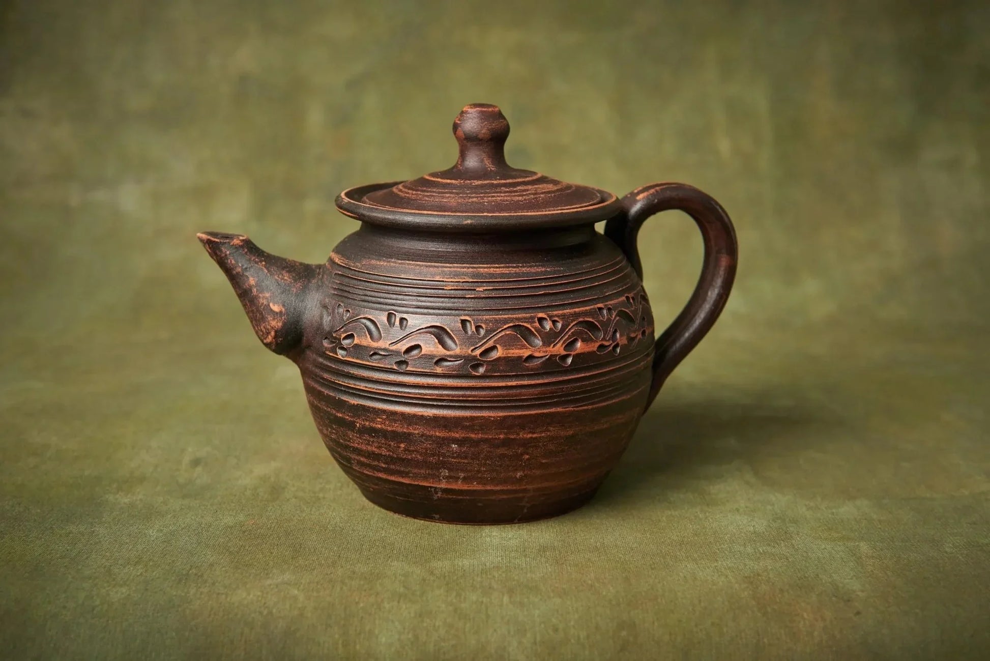 Handcrafted clay teapot with engraved patterns, unique pottery home decor on green background
