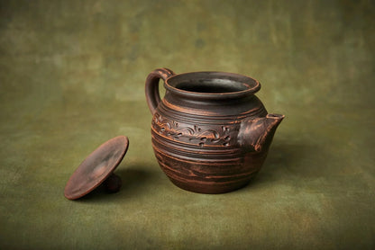 Handmade clay teapot with floral engraving and detached lid on rustic green background