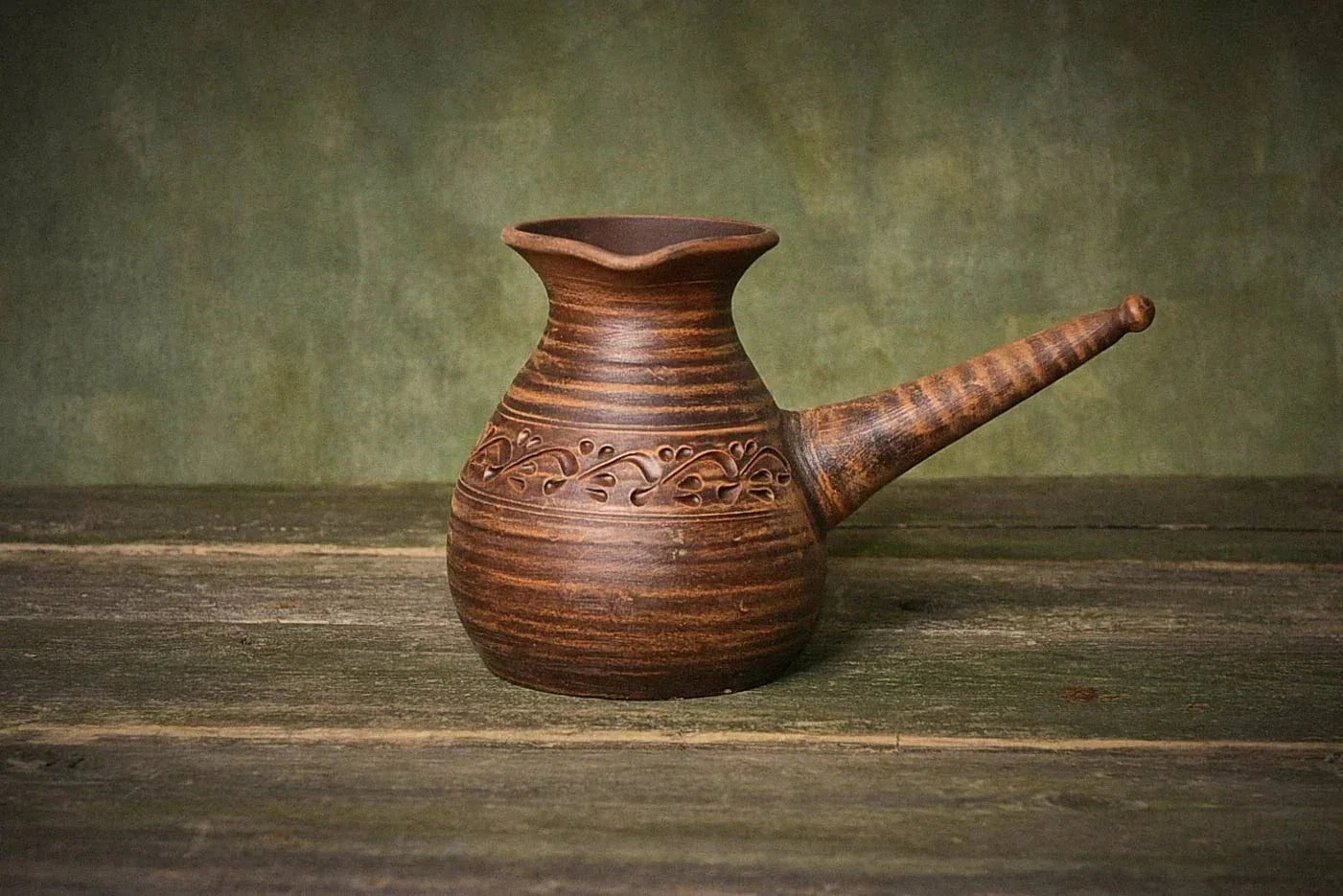 Handmade ceramic cezve coffee pot with decorative handle on rustic wooden surface