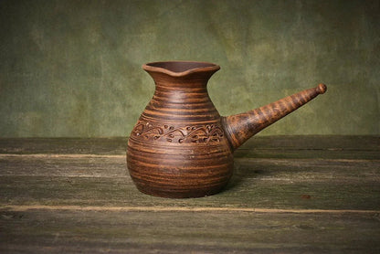 Handmade ceramic cezve coffee pot with decorative handle on rustic wooden surface