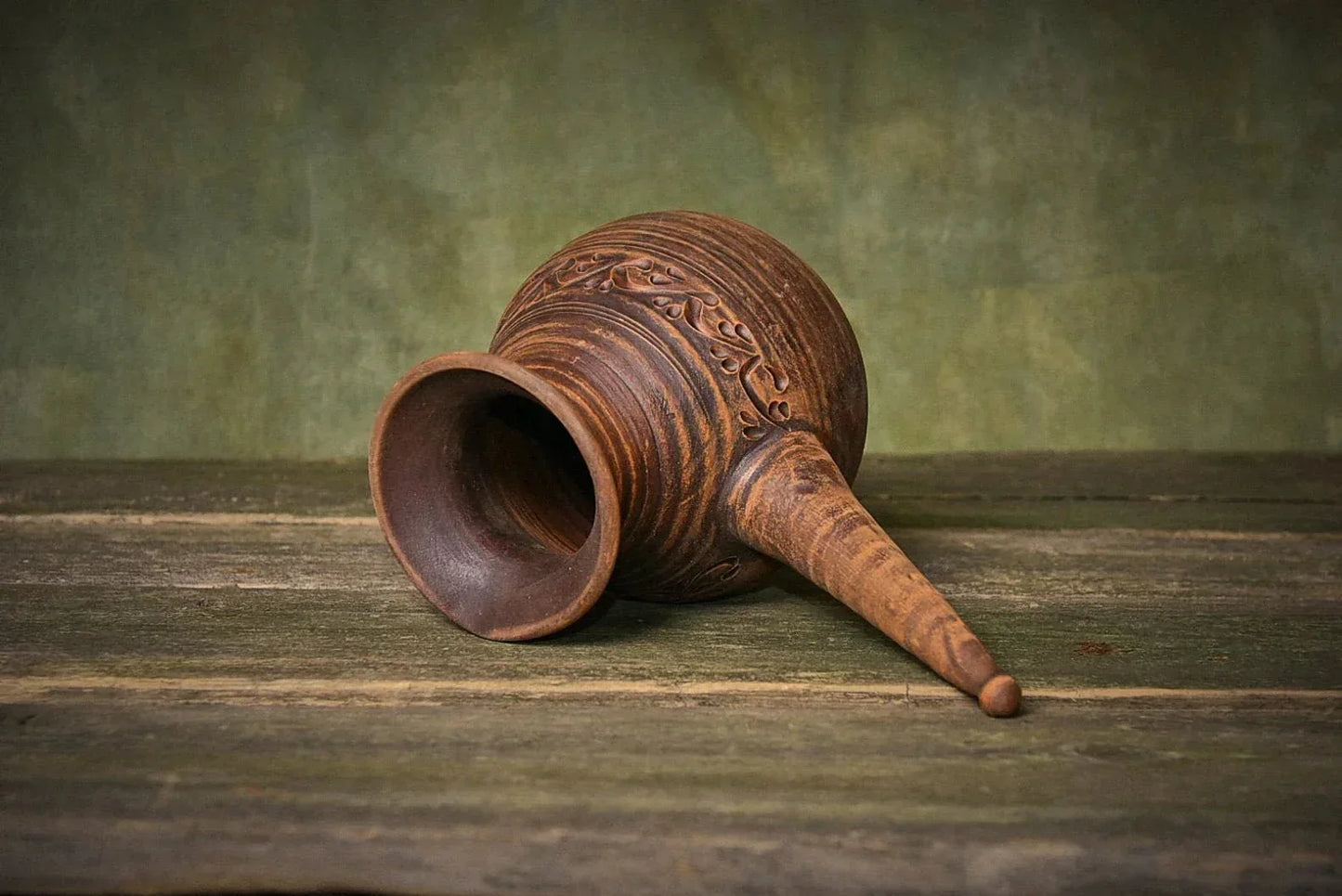 Handmade red clay cezve coffee pot with handle, eco-friendly artisan pottery on rustic wood.