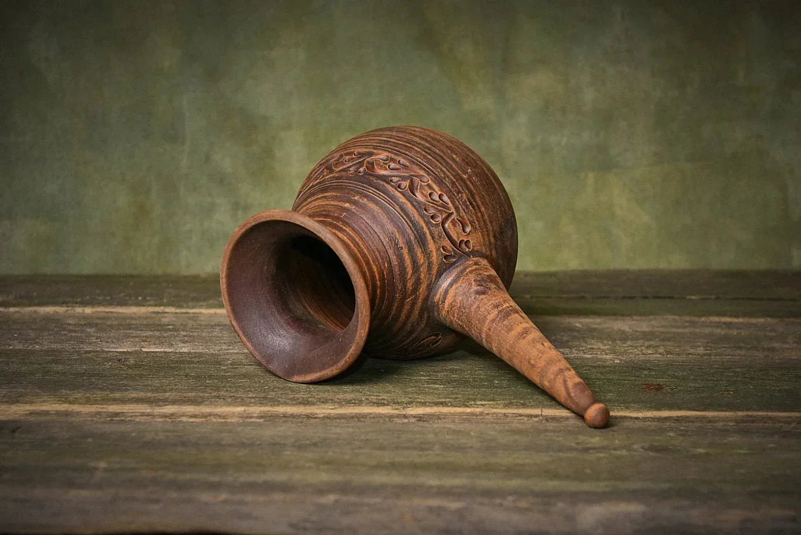 Handmade red clay cezve coffee pot with handle, eco-friendly artisan pottery on rustic wood.