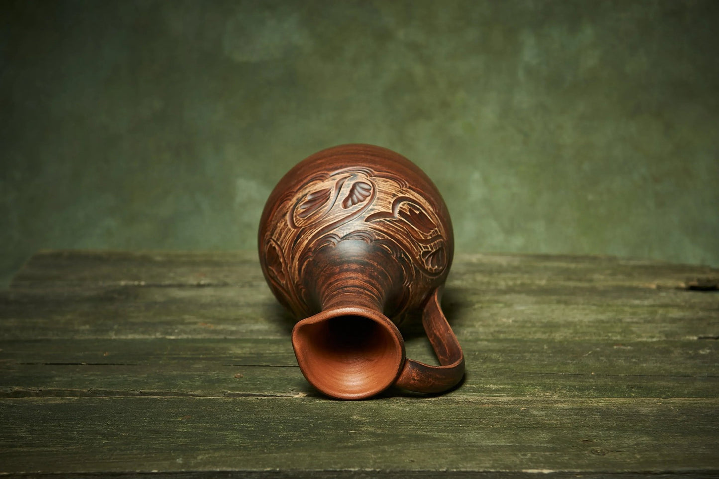 Handmade ceramic pitcher with carved patterns on rustic wood, artisan clay homeware