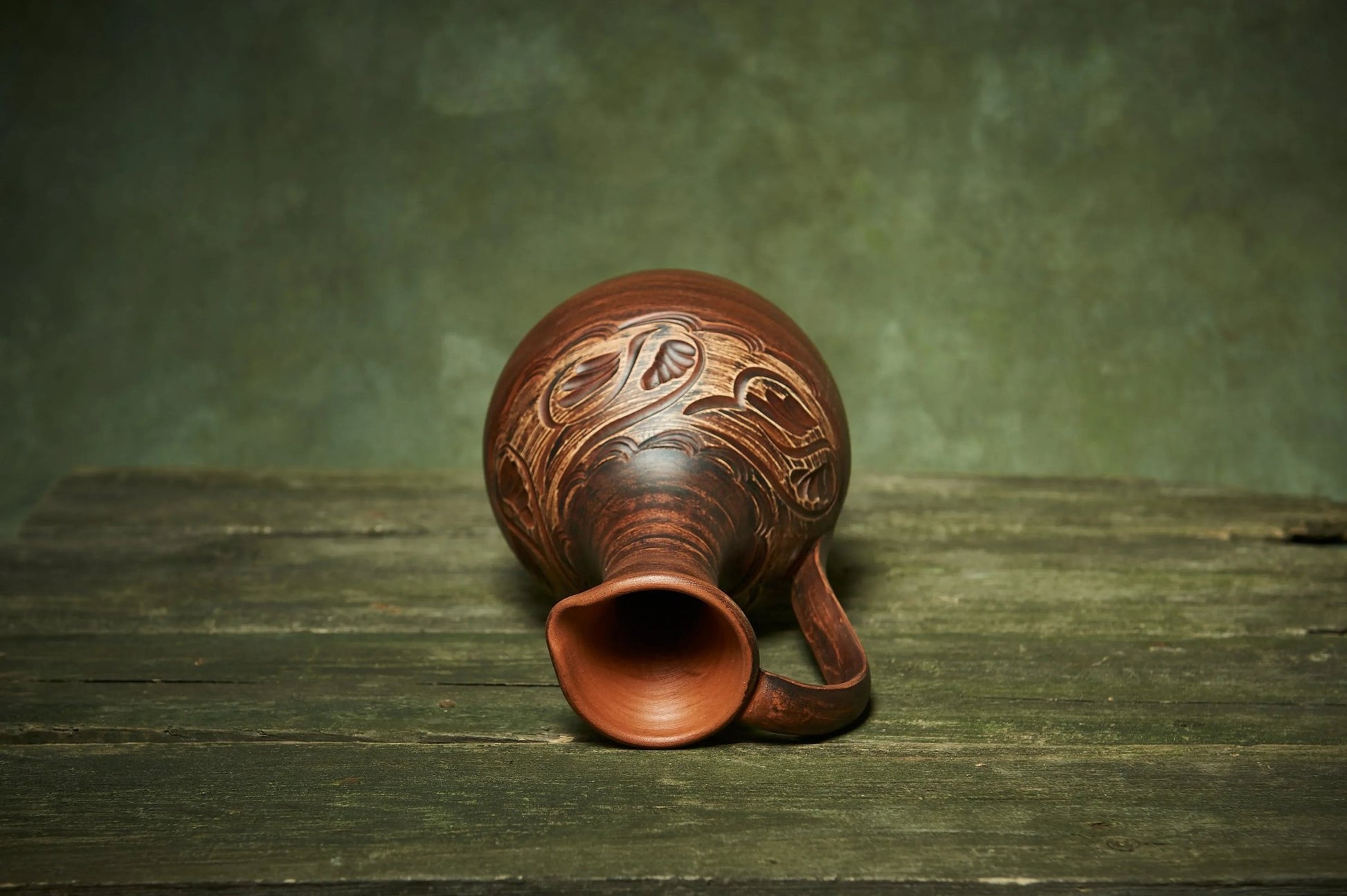 Handmade ceramic pitcher with carved patterns on rustic wood, artisan clay homeware