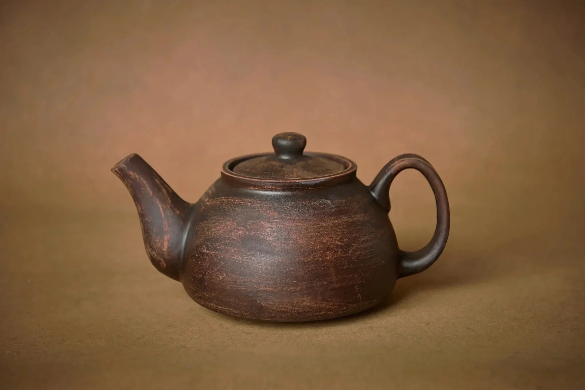 Handmade ceramic teapot, artisan pottery in rustic brown, on a neutral background