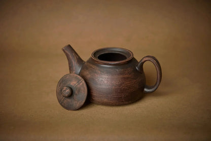 Handmade ceramic teapot with lid, artisanal brown pottery, on a neutral background