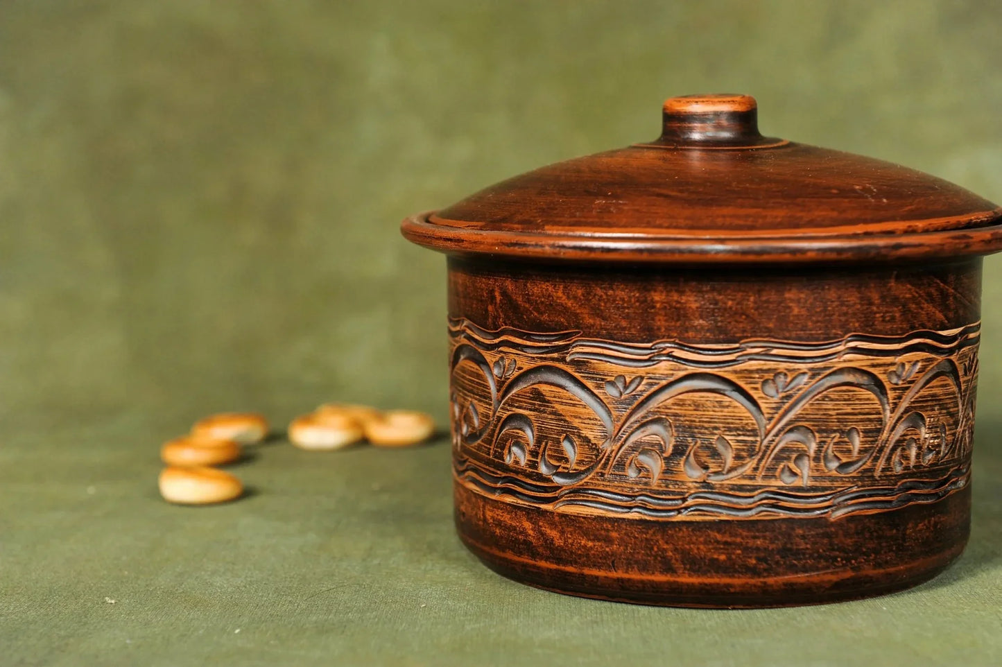 Handmade clay pot casserole with intricate patterns, artisan homeware on green background