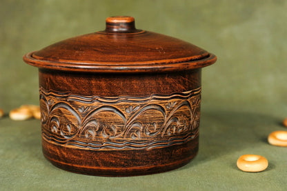 Handmade clay casserole pot with floral carvings, artisan ceramic homeware on green background