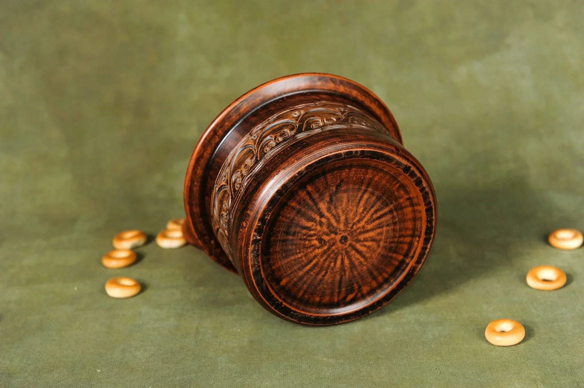 Handmade brown clay pot with detailed carvings on green surface, surrounded by small round bread pieces