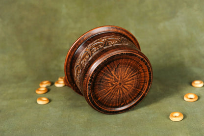 Handmade brown clay pot with detailed carvings on green surface, surrounded by small round bread pieces