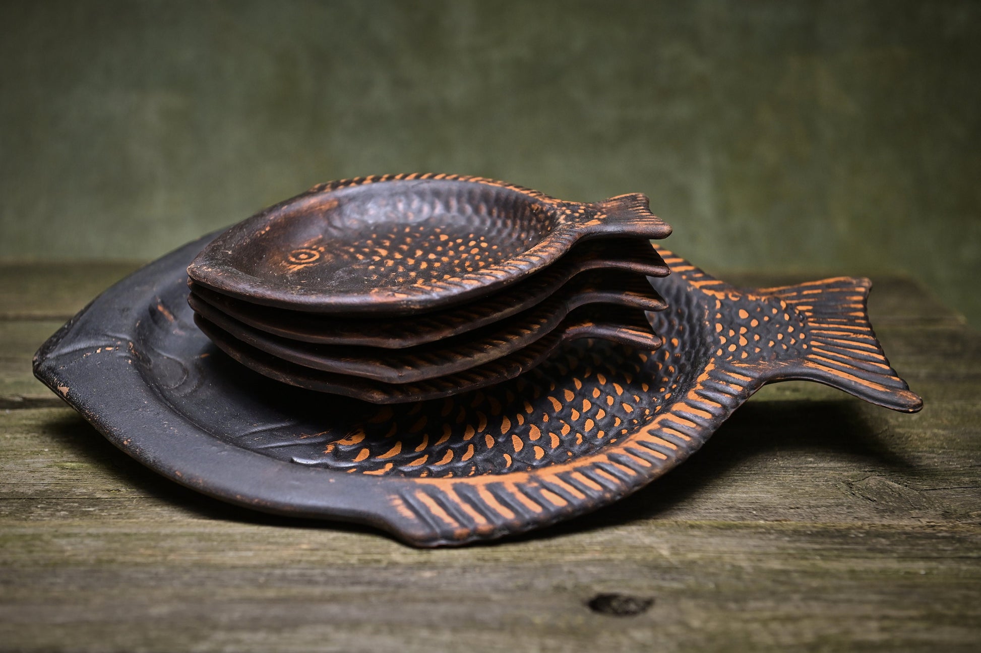 Handmade clay fish-shaped plates stacked on rustic wooden surface, artisan homeware décor