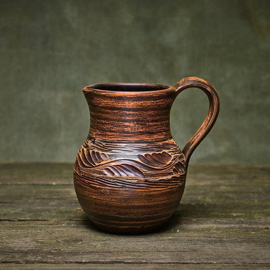 Handmade clay pitcher with carved leaf patterns, rustic brown glaze, artisan-crafted homeware for home décor