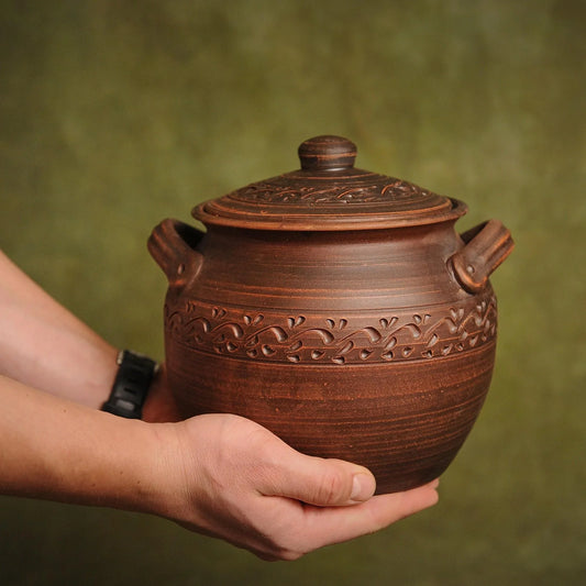Handmade clay pot with carved floral patterns, held in hands, artisan-crafted homeware for rustic décor