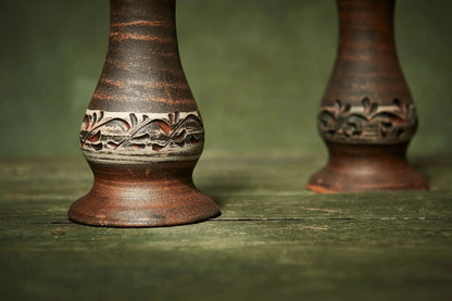 Handmade ceramic candle holders with carved floral design on rustic wooden surface