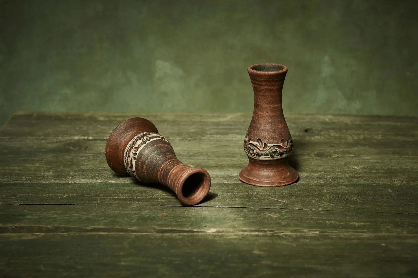Set of two handmade ceramic candlestick holders with carved leaf design on rustic wood table