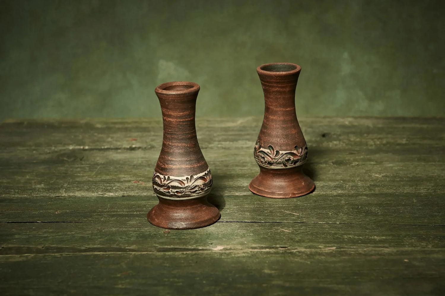 Set of two handmade ceramic candlestick holders with carved floral pattern on rustic wood.
