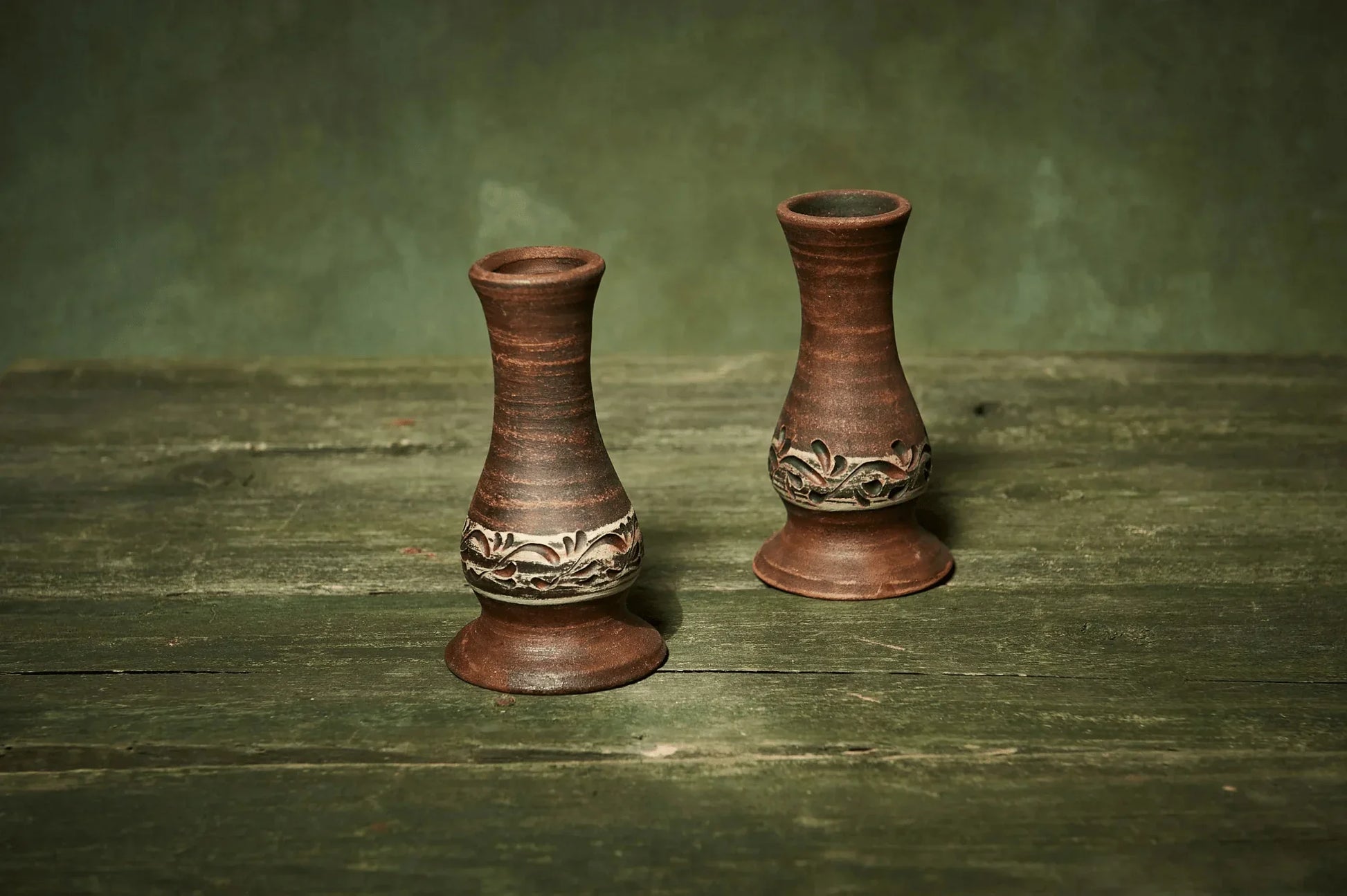 Set of two handmade ceramic candlestick holders with carved floral pattern on rustic wood.