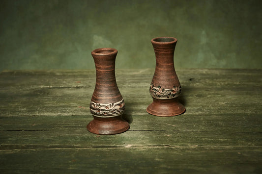 Set of two handmade ceramic candlestick holders with carved floral pattern on rustic wood.