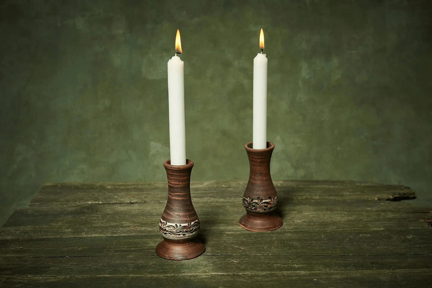 Set of two handmade ceramic candlestick holders with white candles on rustic wood table