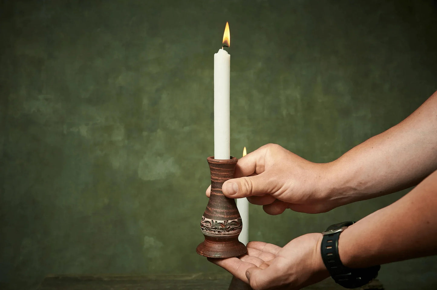 Hand holding handmade ceramic candle holder with lit white candle, artisan clay homeware