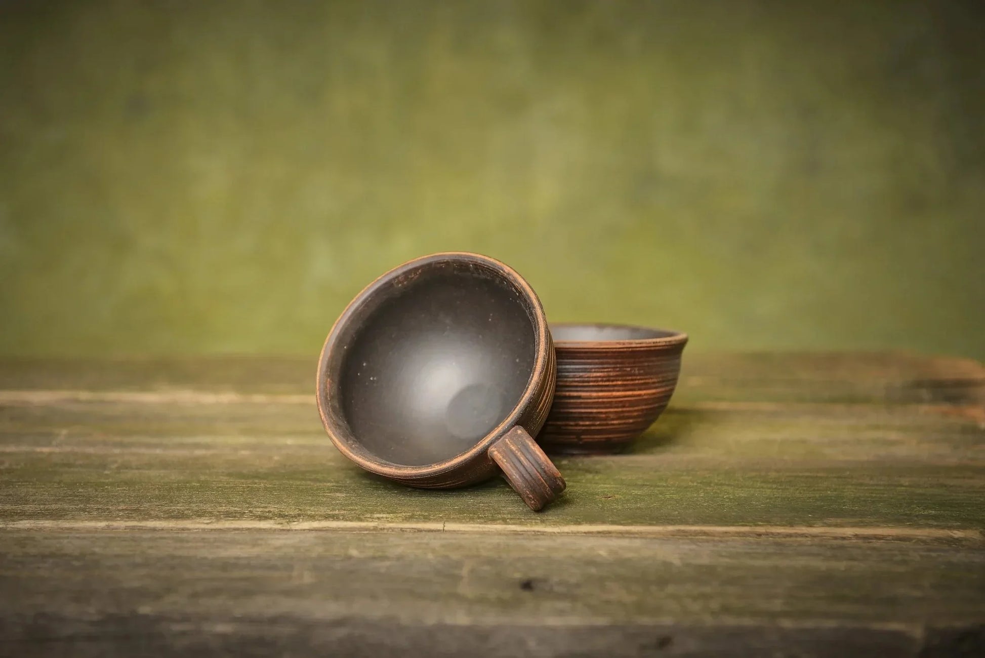 Set of two handmade ceramic clay mugs on rustic wooden surface, artisanal pottery homeware