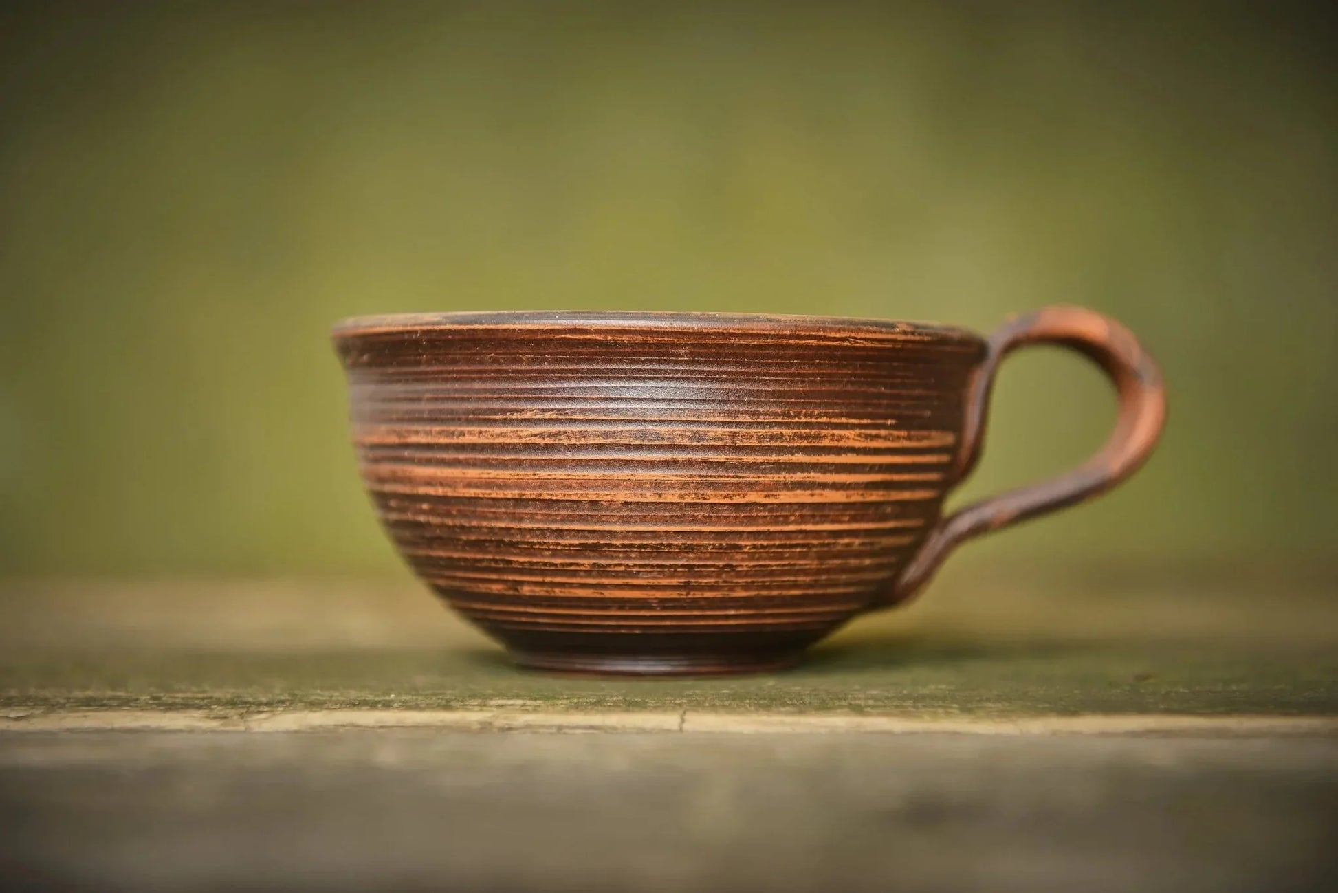 Handmade ceramic clay mug with textured brown finish on rustic wooden surface