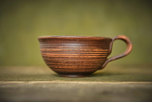 Handmade ceramic clay mug with textured brown finish on rustic wooden surface