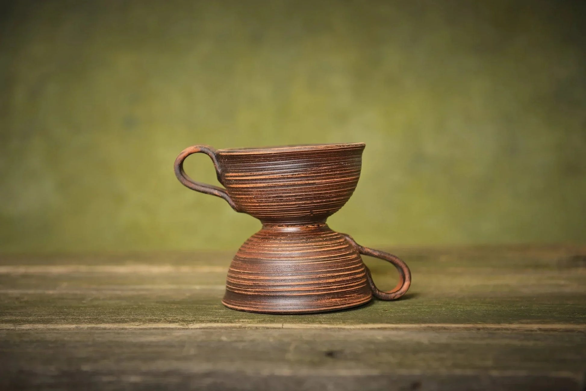 Set of two handmade ceramic clay mugs stacked, artisanal pottery on wooden surface.