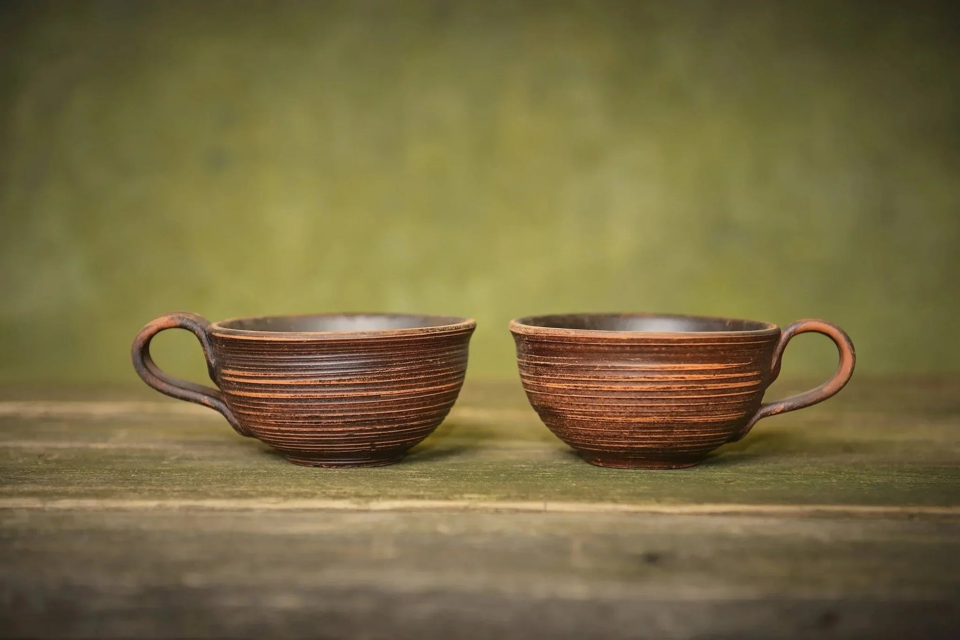 Set of two handmade ceramic clay mugs with textured brown finish on rustic wood table