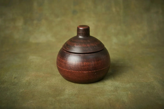 Handmade small ceramic clay baking pot with lid on green background, artisan homeware