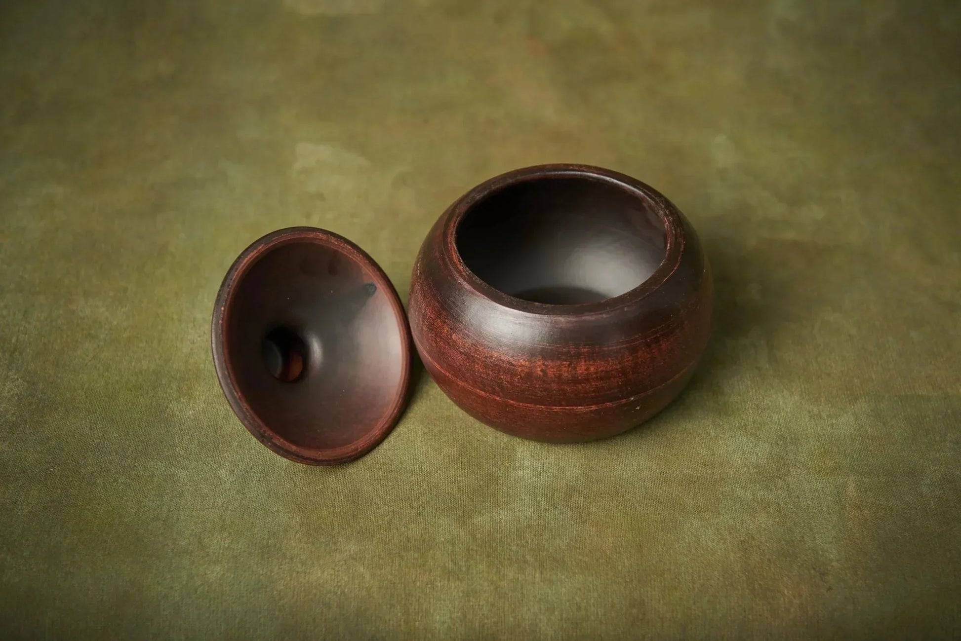 Handmade small brown ceramic baking pot with lid on green surface, artisan clay cookware.