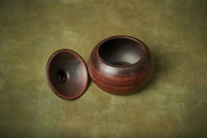 Handmade small brown ceramic baking pot with lid on green surface, artisan clay cookware.
