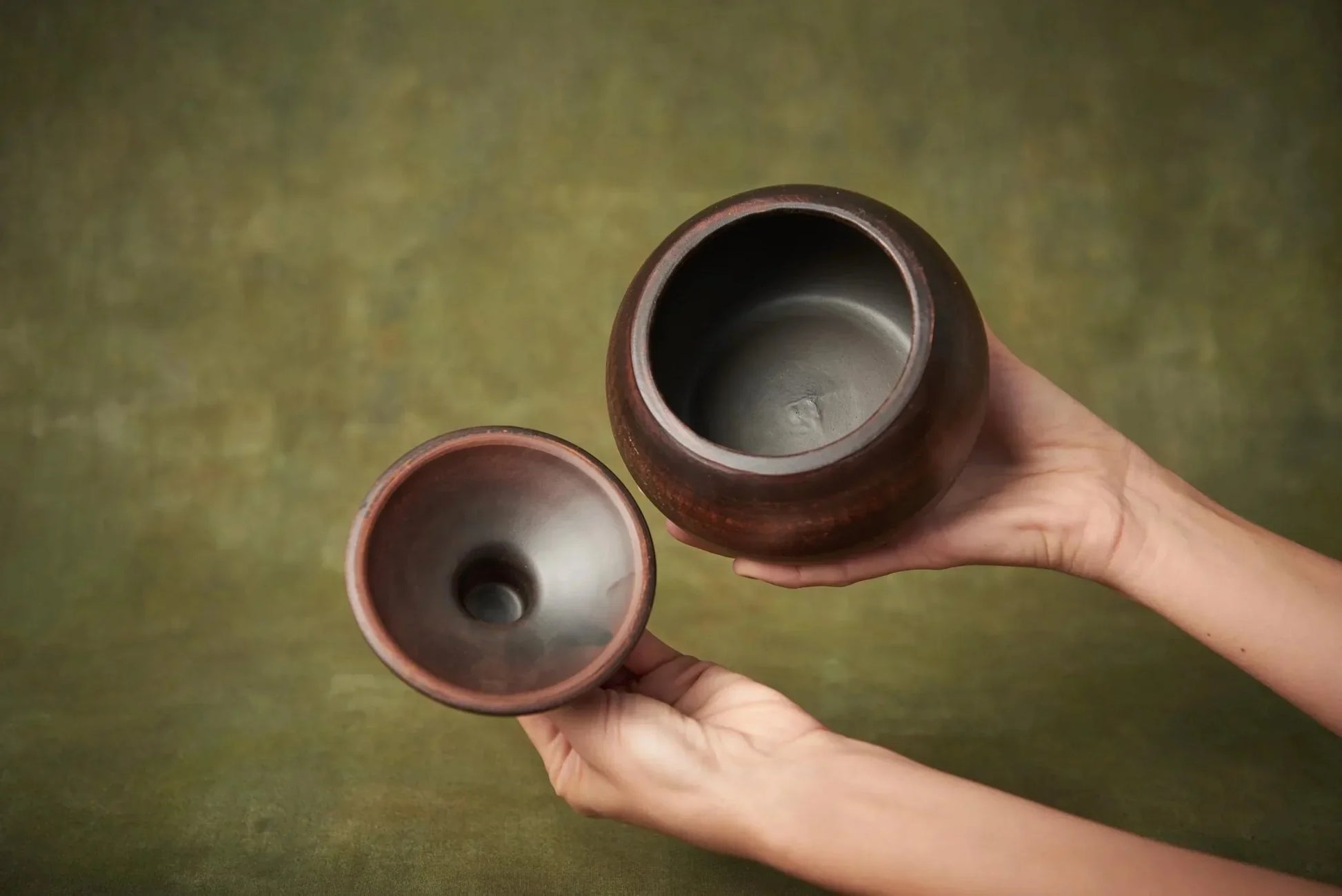 Hand holding small handmade clay casserole pot with lid, artisan stoneware bakeware