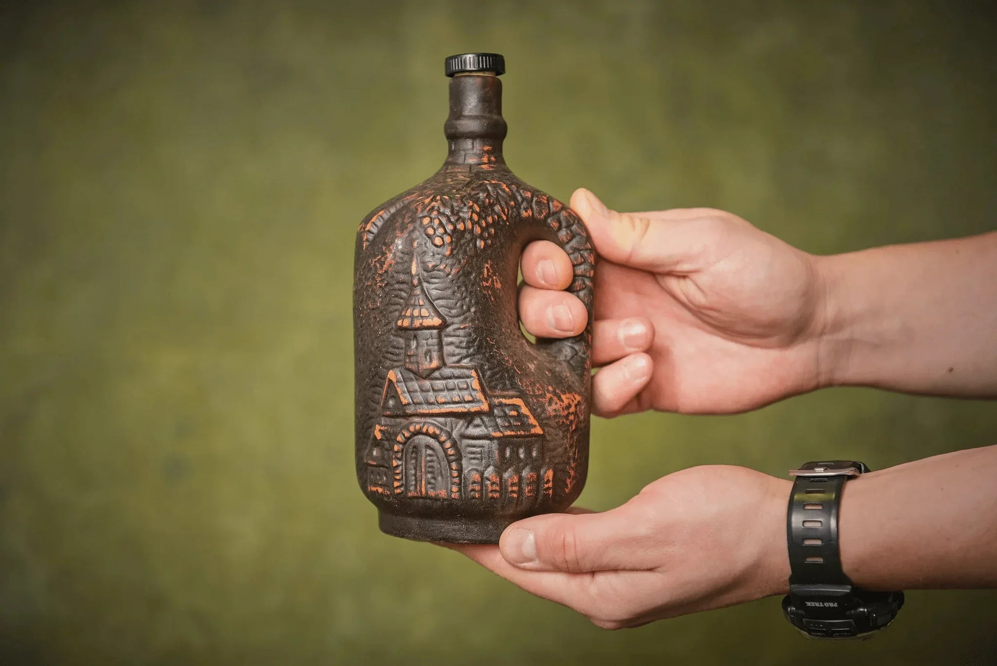 Hand holding a small handmade ceramic clay jug with rustic relief design, country decor