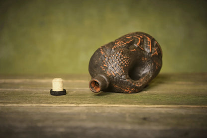 Handmade small ceramic clay bottle with cork on rustic wooden surface for home decor