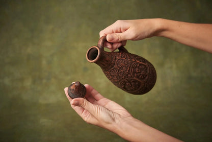 Handmade clay pitcher with ornate lid, rustic farmhouse decor, held by two hands