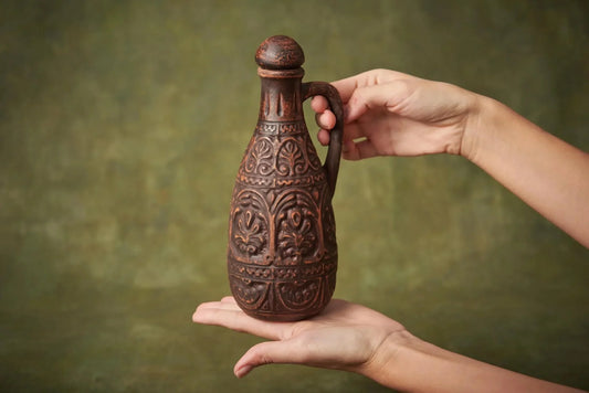 Hand holding ornate small ceramic clay pitcher jug with lid, farmhouse kitchen decor