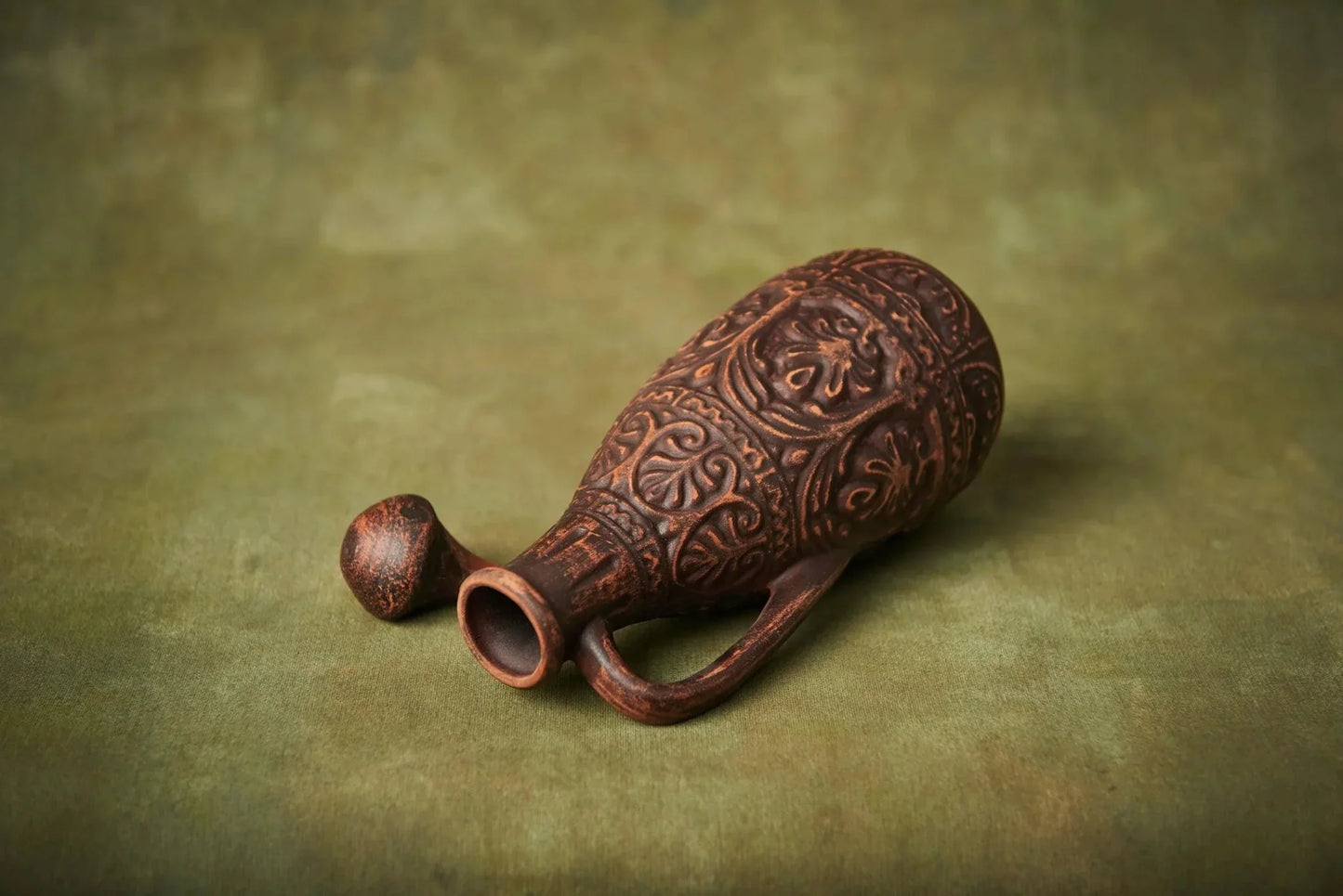 Handmade small ceramic clay jug with intricate patterns and lid on a green background