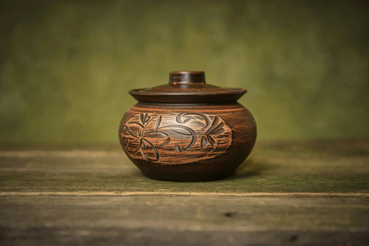 Handmade ceramic sugar bowl with lid and floral engraving on rustic wood surface