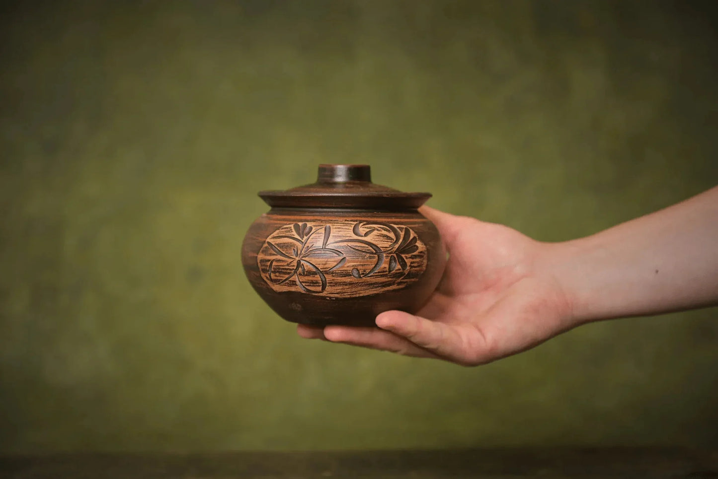 Hand holding handmade ceramic sugar bowl with lid, floral carving, artisan clay homeware
